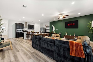 Un soggiorno moderno con un divano scuro, una TV e una parete verde a contrasto.