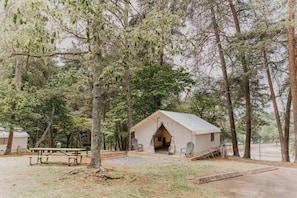 Un alloggio in tenda con tavolo e sedie da picnic, immerso tra gli alberi.