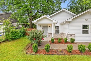 A single-story house with a front porch, a small front yard with shrubs, and a tree to the left. - Modern 4BHK Backyard 25 mins FIFA 10 mins Downtown (Dallas)