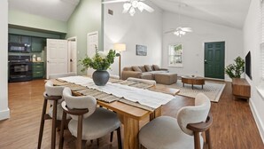 Un grand espace de vie comprenant une table à manger, des chaises, un canapé, un téléviseur et un ventilateur de plafond.