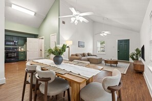 Ein geräumiger Wohnbereich mit Esstisch, Stühlen, einer Couch, einem Fernseher und einem Deckenventilator.
