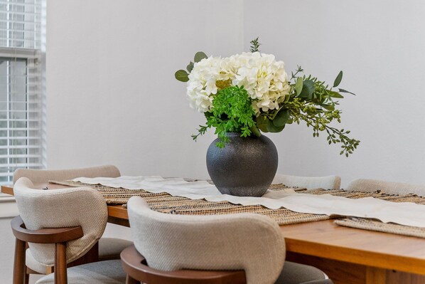 Ein Esstisch mit einer Vase weißer Blumen, gewebten Platzsets und modernen Stühlen.