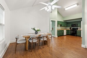 A dining area with a table and chairs, a ceiling fan, and a kitchen with green cabinets and appliances. - Modern 4BHK Backyard 25 mins FIFA 10 mins Downtown (Dallas)