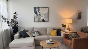 En stue med sofa, sofabord, lampe og et maleri på væggen.
