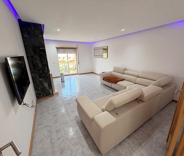 Ein modernes Wohnzimmer mit einer Eckcouch, einem Flachbildfernseher und einer Wand mit Marmorverkleidung.
