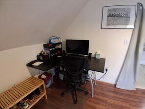 Et værelse med skrivebord, stol, fjernsyn og et billede i ramme på væggen.