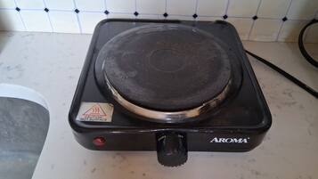Um fogão elétrico preto com um aviso de segurança, um botão de controle e a marca 'AROMA' em uma bancada de cozinha.