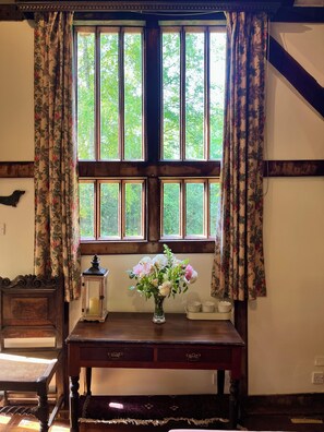 A room with a large window, a wooden table with a vase of flowers, and a small lantern.