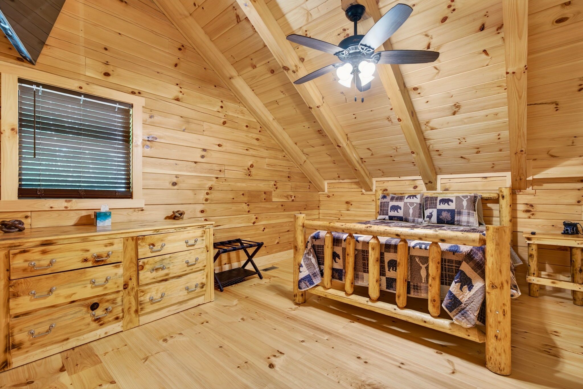 Un intérieur en bois comprenant un lit, une commode, une fenêtre avec des stores et un ventilateur de plafond.