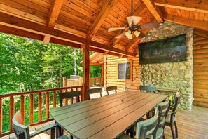 Um deck de madeira com mesa e cadeiras, uma parede de pedra com um quadro e um ventilador de teto.