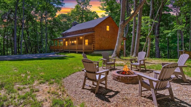Une cabane en bois avec un porche, entourée d’arbres, et un espace extérieur aménagé avec un foyer.