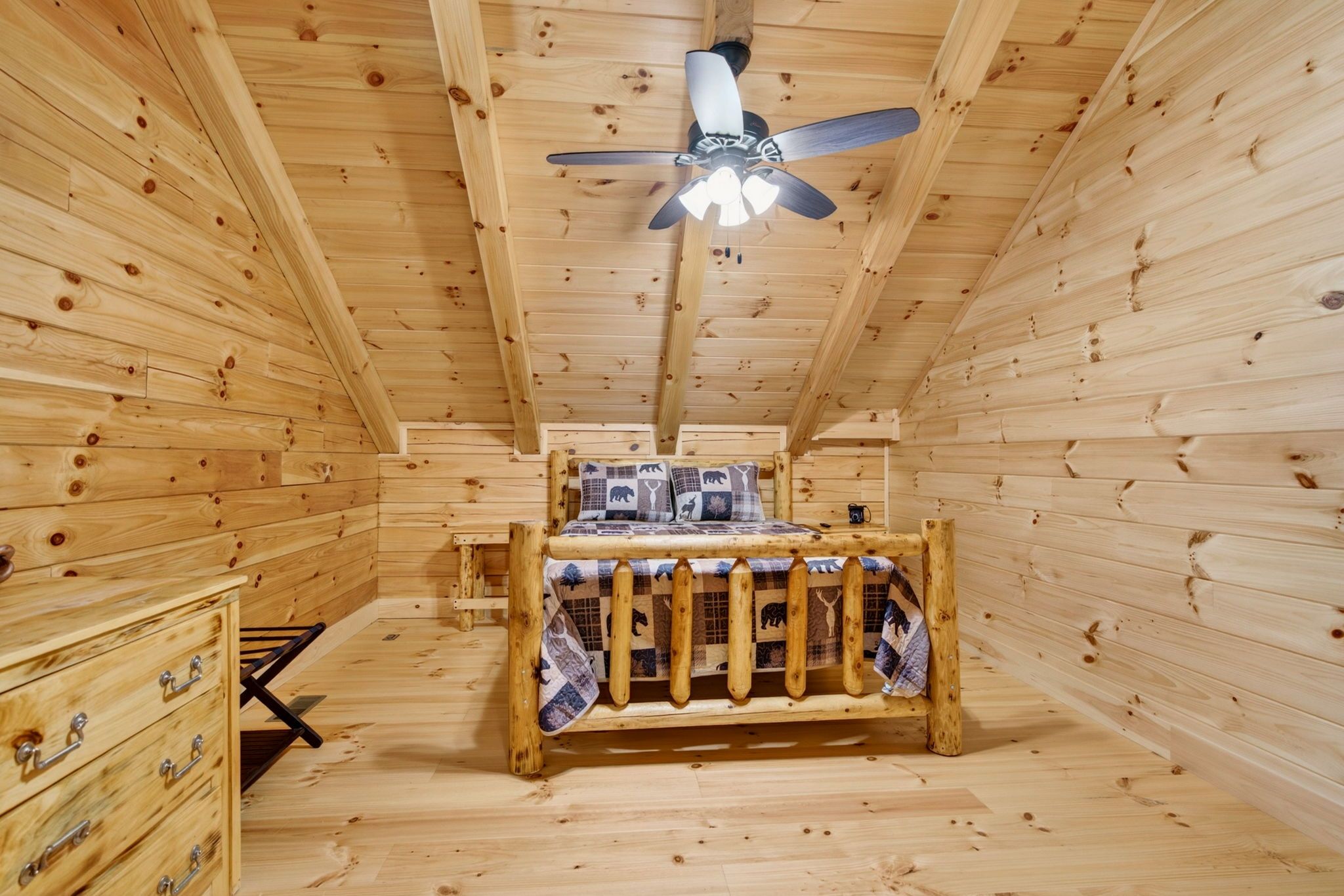 Une chambre dans un chalet en bois, avec un lit, une commode et un ventilateur de plafond.