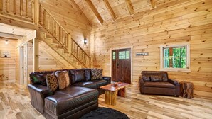 L’intérieur d’une cabane est agrémenté d’un escalier en bois, de canapés en cuir, d’une table basse en bois et d’une fenêtre donnant sur la forêt.