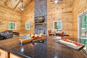A wooden cabin interior with a stone fireplace, a dining area, and a large kitchen island. - Happy Hours Cabin/Hot Tub & Hocking Hills (Logan)