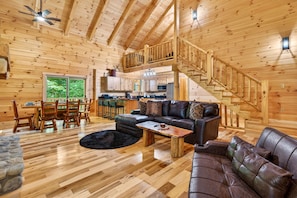 A wooden cabin interior with a dining area, a living room with a sofa and coffee table, a kitchen, and a staircase. - Happy Hours Cabin/Hot Tub & Hocking Hills (Logan)