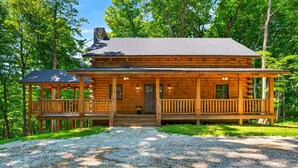 Une cabane en rondins avec un porche, une cheminée et une allée gravillonnée.