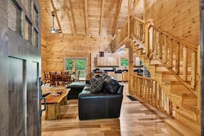 L’intérieur d’une cabane en rondins comprend un coin repas, un canapé, un escalier et une cuisine.