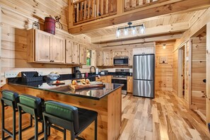 Eine holzgetäfelte Landhausküche mit Kochinsel, Barhocker und modernen Geräten.