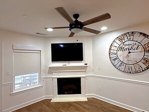 Ein Wohnzimmer mit Kamin, einem an der Wand befestigten Fernseher, einem Deckenventilator und einer großen Wanduhr.