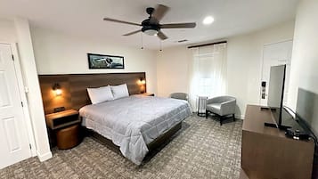 A hotel room with a bed, a desk, a chair, a ceiling fan, and a TV.