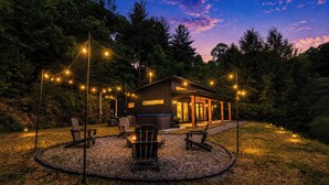 Une cabane dotée d’une terrasse, entourée d’arbres, et illuminée de guirlandes lumineuses.