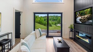 Un salon moderne comprenant un canapé, une table basse, une cheminée et une grande fenêtre donnant sur un paysage verdoyant.