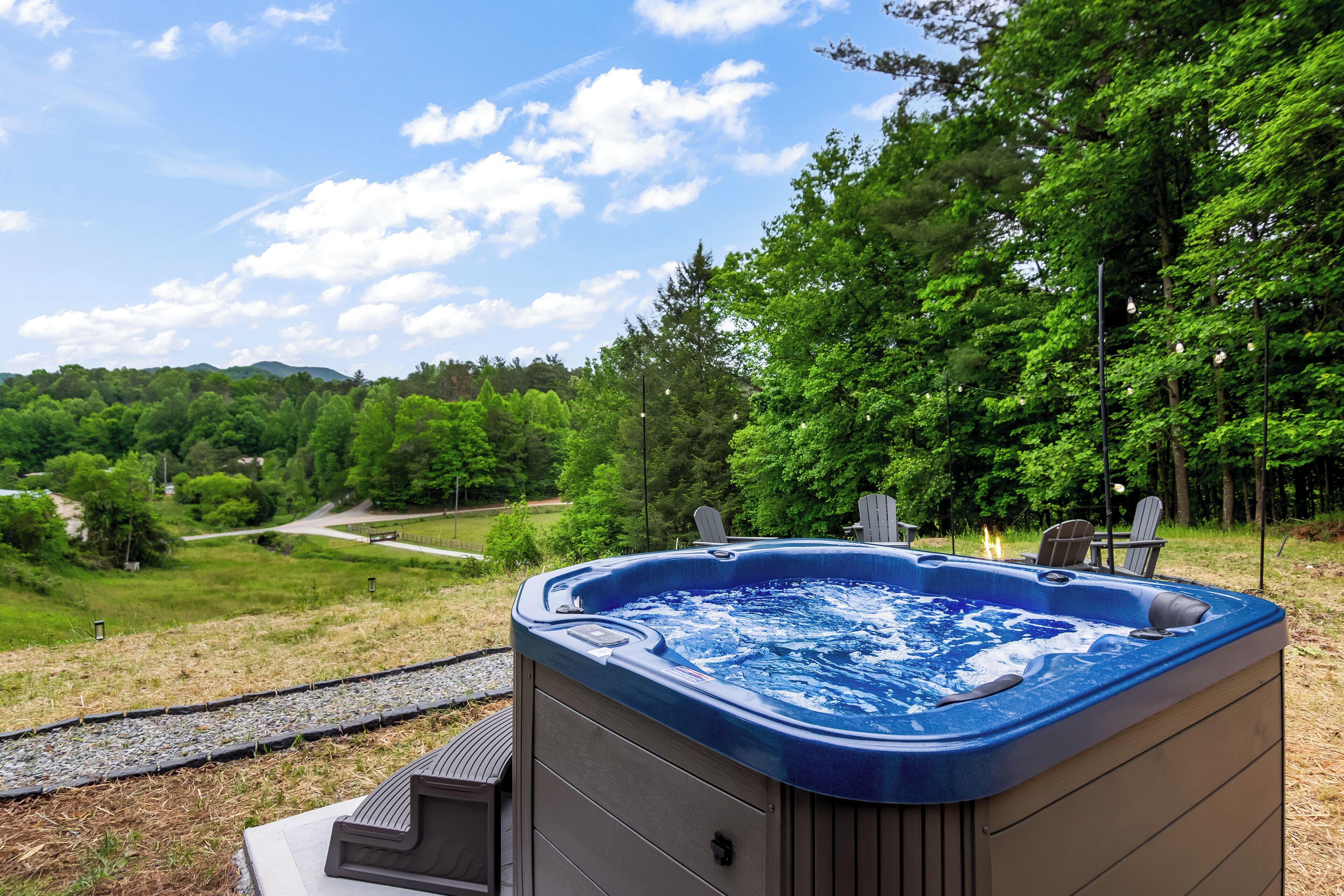 A hot tub with a view of a forest and a pathway.