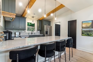 A modern kitchen with a large island, bar stools, and a view of a mountainous landscape. - Brand New Luxe Modern Cabin: Views, Hot tub, Creek (Ellijay)