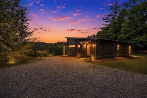 A modern cabin with a gravel driveway, surrounded by trees and a clear sky. - Brand New Luxe Modern Cabin: Views, Hot tub, Creek (Ellijay)