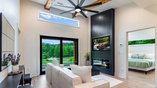 Un salon moderne avec un canapé, une cheminée, un téléviseur et un balcon offrant une vue sur la verdure.
