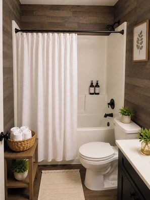 Ein Badezimmer mit Duschvorhang, Toilette, Badewanne, Waschbecken, einer Handtuchkorb und einer kleinen Pflanze.