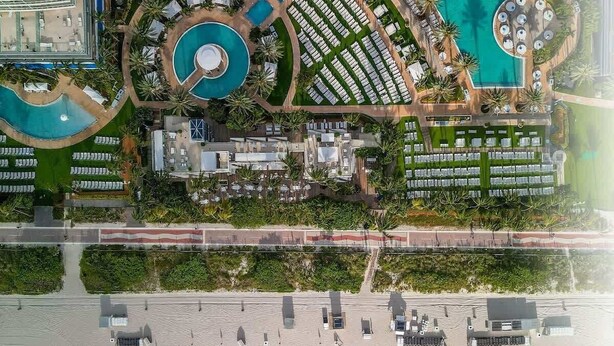 Luftaufnahme eines Resorts mit mehreren Schwimmbecken, einem Strandbereich und einer Strandpromenade.