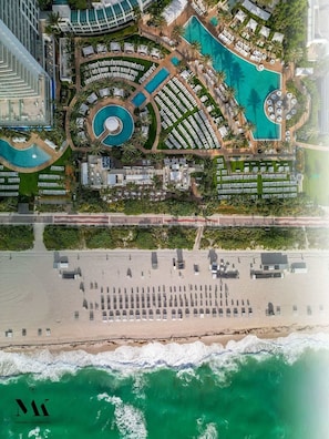 An aerial view of a resort with multiple swimming pools, a beach area, and a beachfront promenade. - Fontainebleau | 1BR Beachfront Haven + Spa Passes (Miami Beach)