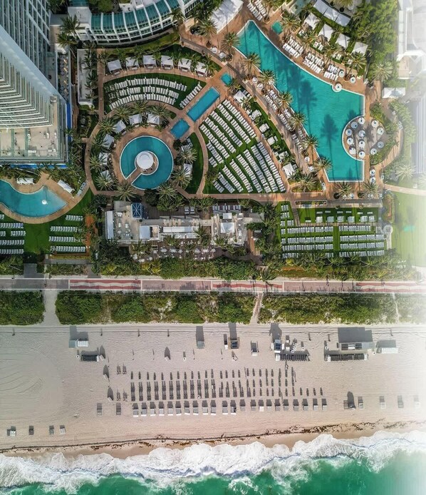 Ein Luftbild eines Resorts mit mehreren Schwimmbecken, einem Strandbereich und einem Parkplatz.