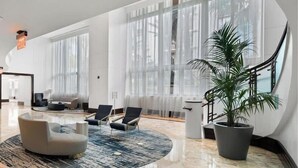Um lobby moderno com uma escadaria curva, janelas amplas e um vaso de planta.