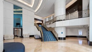 Um hall amplo com escadaria central, balcão de recepção e área de estar.