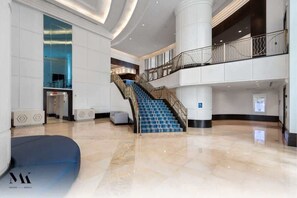 Eine geräumige Lobby mit einer zentralen Treppe, einem Empfangsbereich und einer Sitzecke.