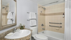 Ein Badezimmer mit Waschbecken, Toilette und Badewanne, ausgestattet mit Haltegriffen und einer Duschbrause.