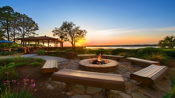 A patio with a fire pit, benches, and a gazebo overlooking a body of water at sunset. - Hilton Head Island Escape with Spacious 2BR Villa Near the Beach (Hilton Head Island)