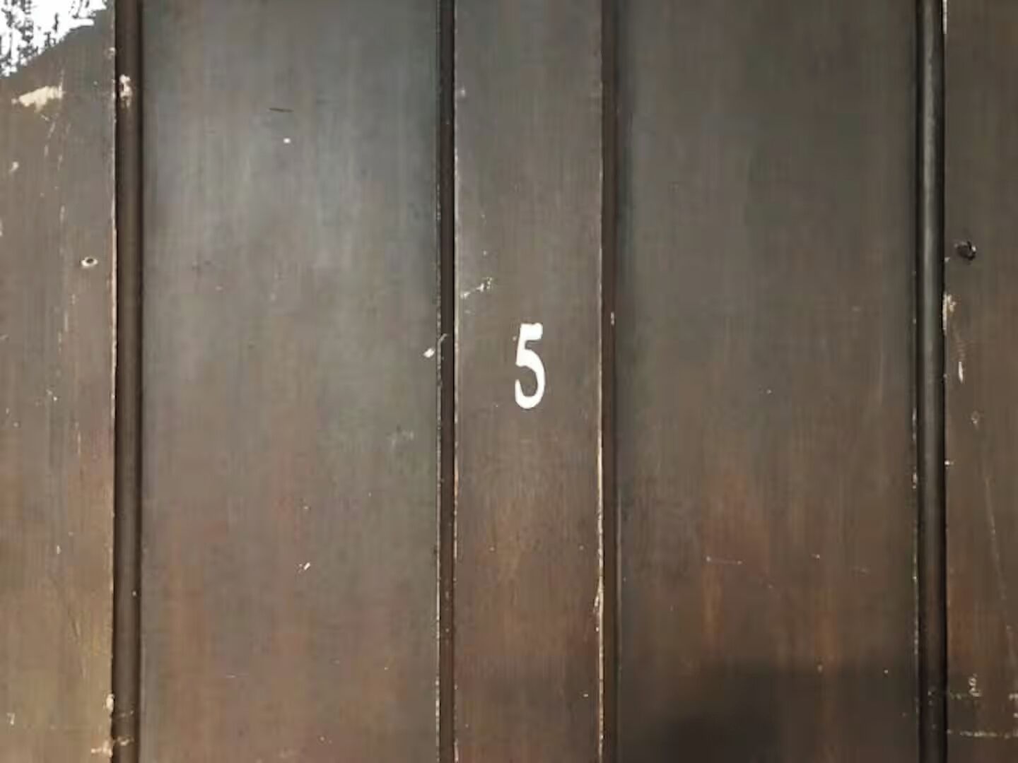 A dark wooden door with the number '5' painted on it.