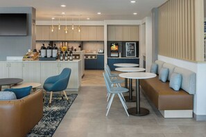 Una cucina moderna con isola centrale, zona bar, posti a sedere con divano e poltrone, e angolo pranzo con tavoli rotondi.