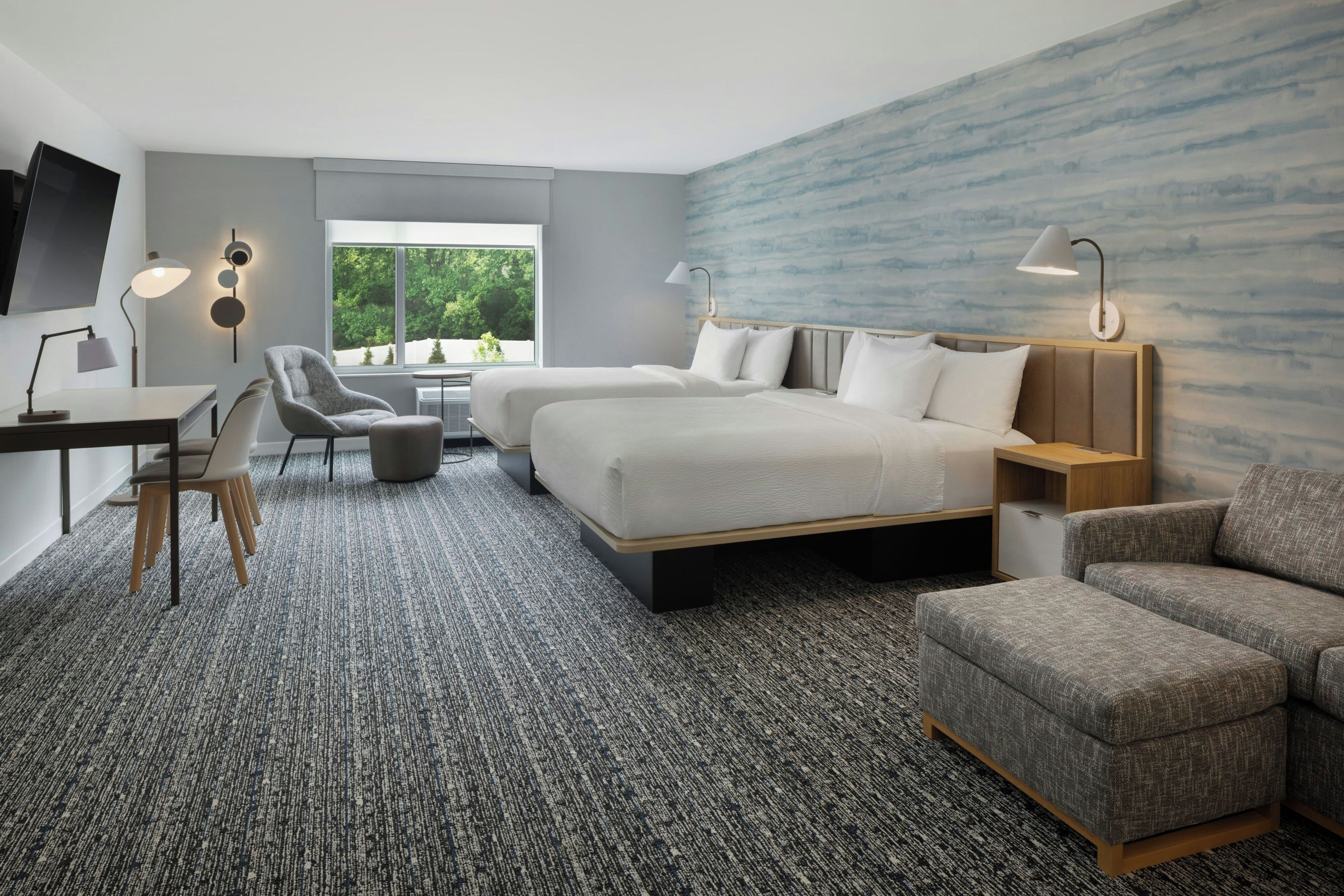 A modern hotel room with a large bed, a desk, a chair, and a sofa.