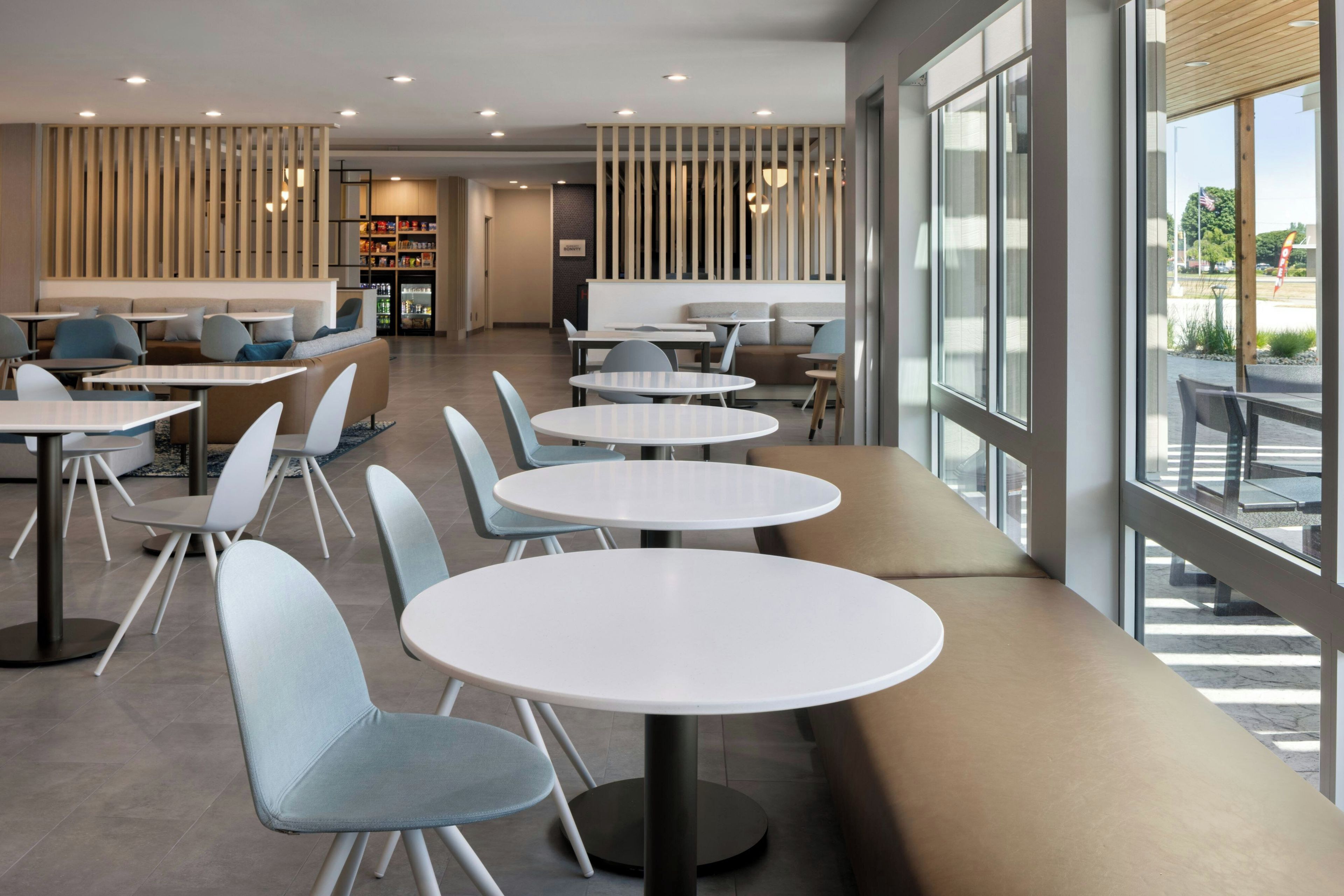 A modern cafe interior with round tables, cushioned seating, and a view through large windows.