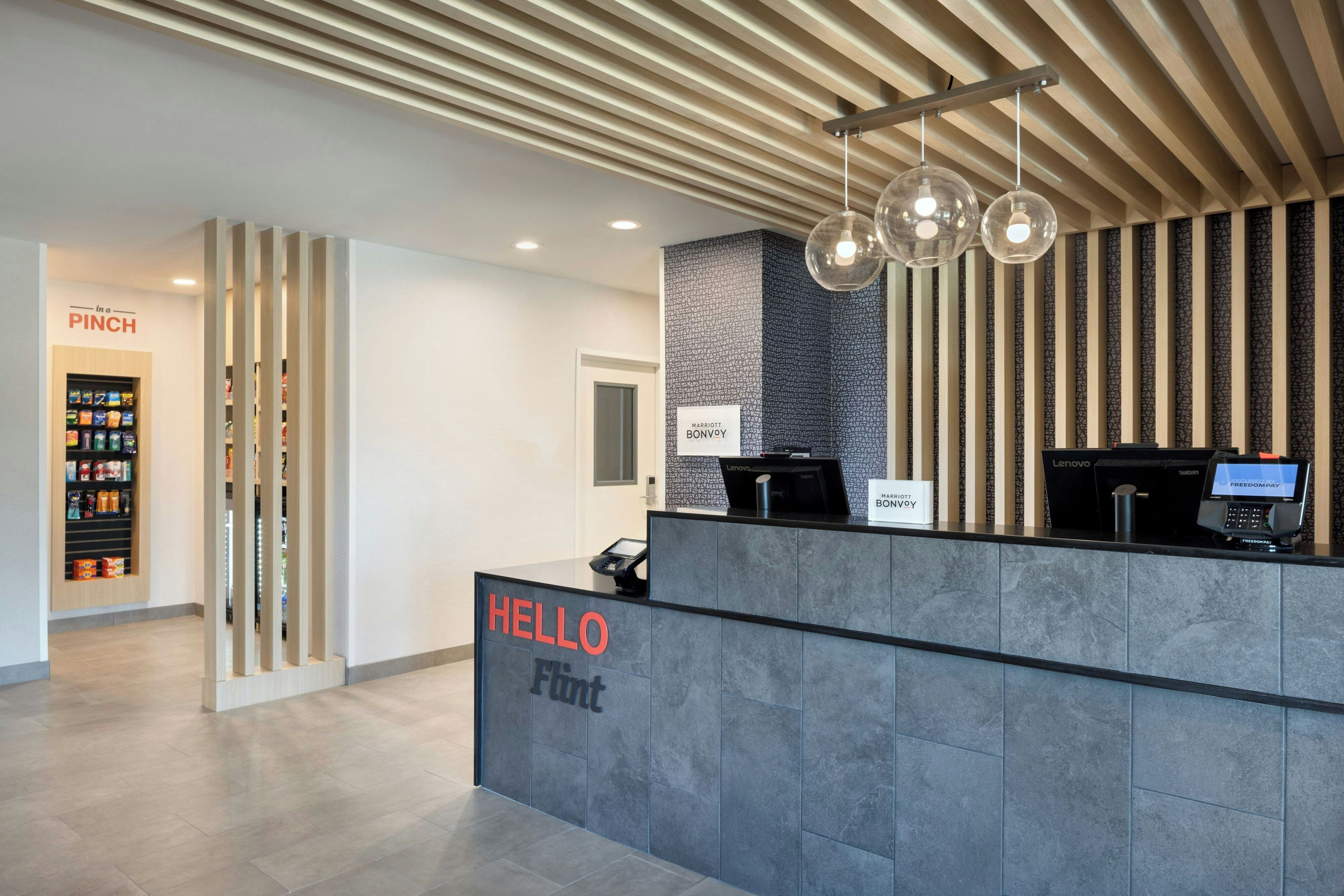 A hotel reception desk with a 'HELLO' sign, a 'Marriott Bonvoy' sign, and a 'Lenovo' branded computer.