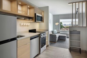 Una cucina moderna con elettrodomestici integrati, un'area pranzo con divano grigio e vista attraverso una finestra.