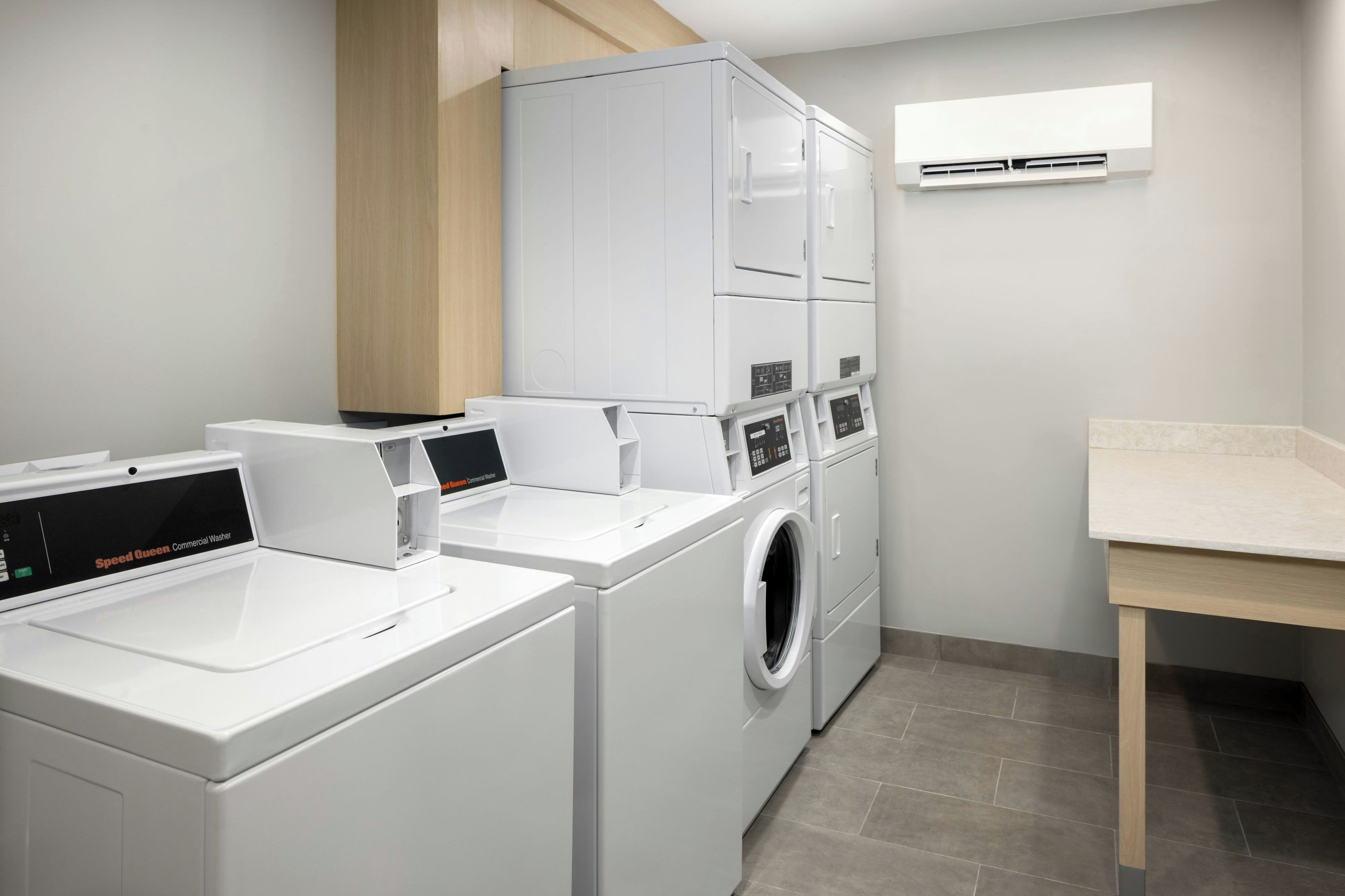 A laundry room with stacked washers and dryers, a countertop, and an air conditioning unit.