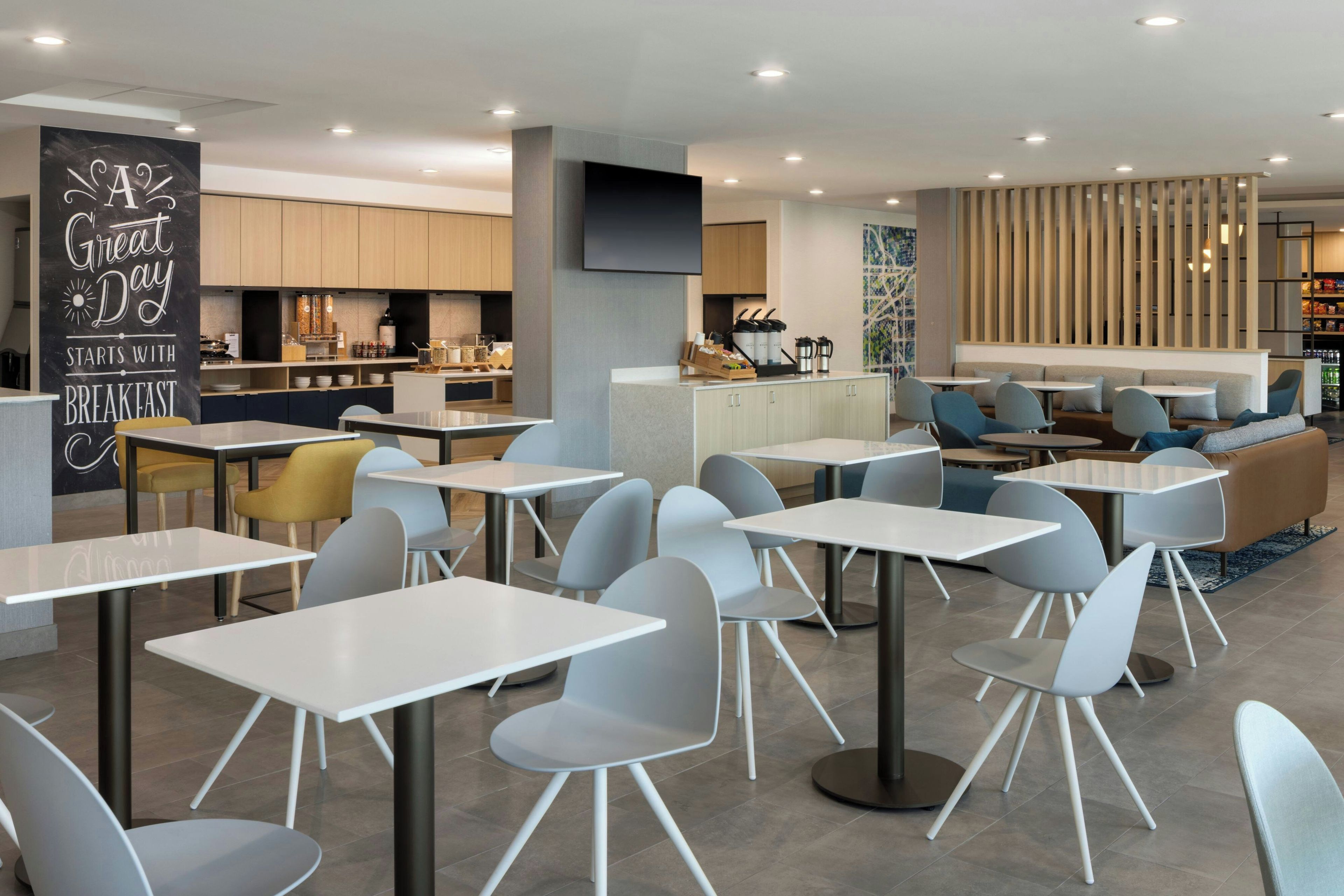 A modern cafe with tables and chairs, a kitchen area, and a seating area with a view.