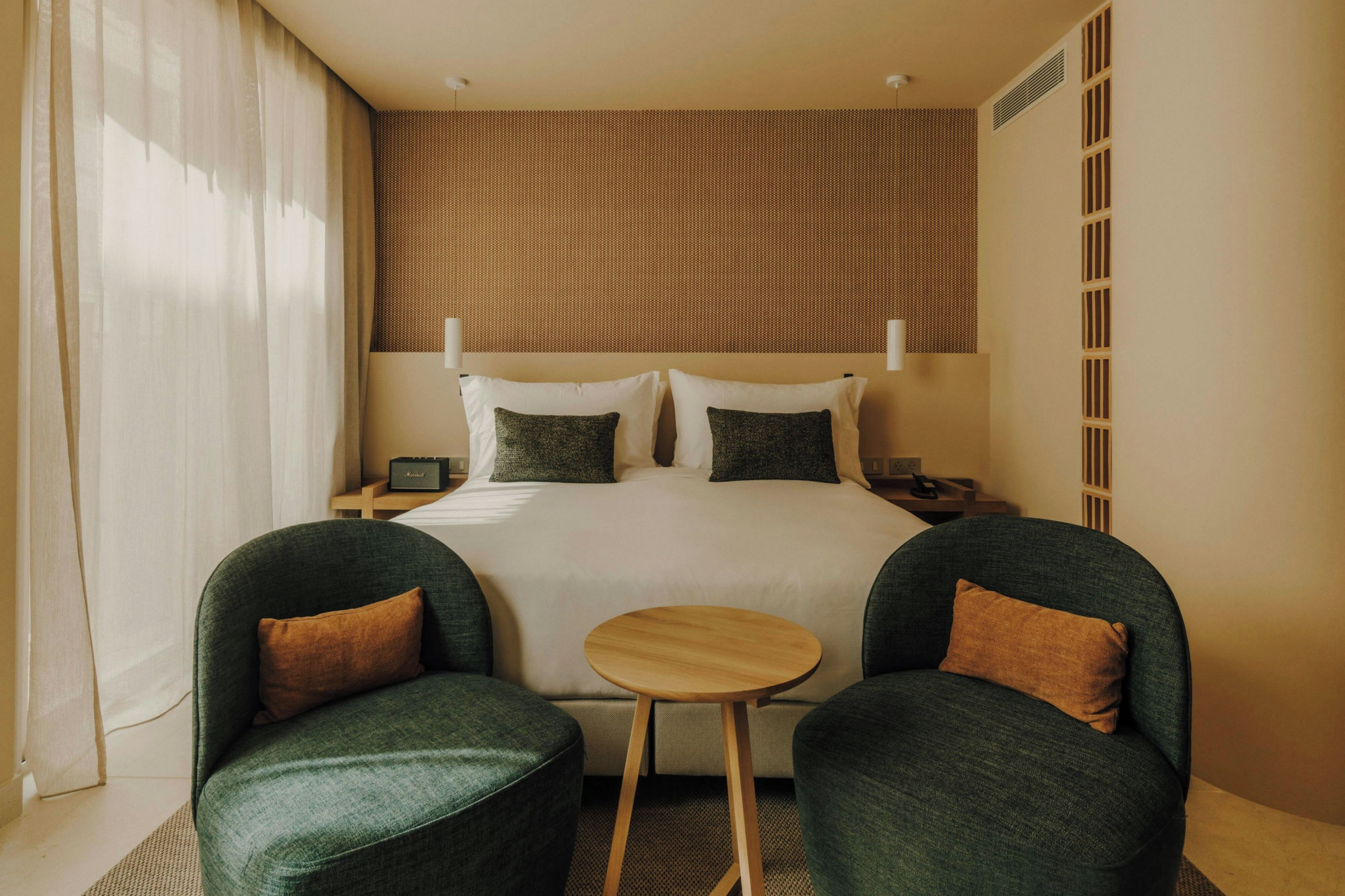 Habitación de hotel con una cama grande, dos sillones, una mesita redonda y un cabecero con diseño estampado.