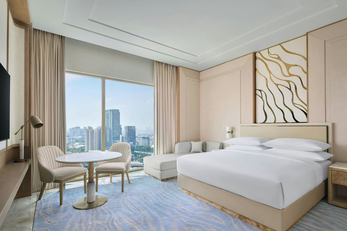 A hotel room with a large bed, a sofa, a small table, and a TV.