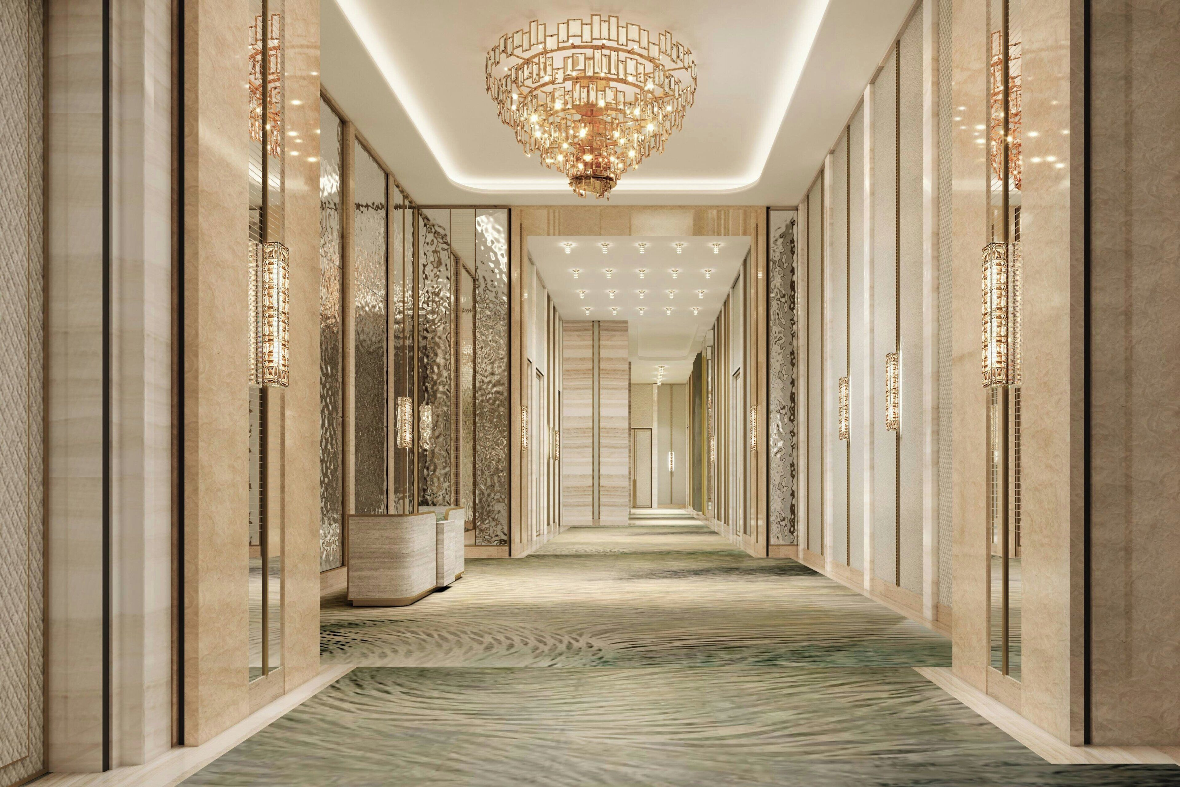 A corridor with a patterned carpet, a chandelier, and mirrored walls.